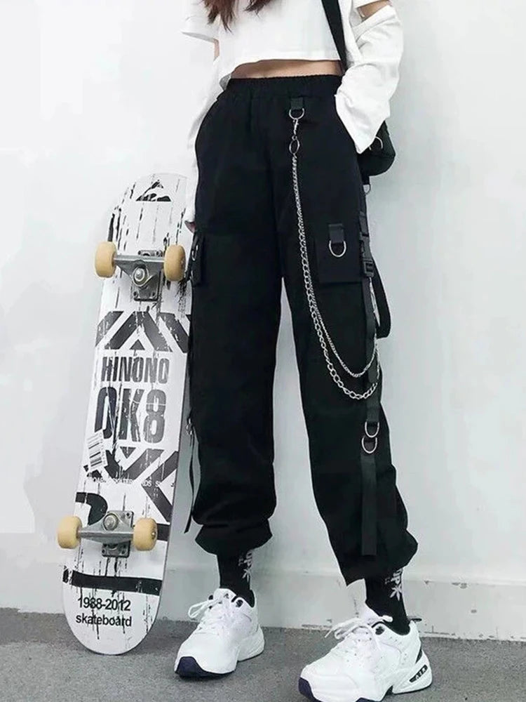 Woman wearing black Harajuku-inspired high-waist cargo joggers with chain and pocket details, styled with sneakers and a skateboard.